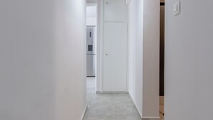 A hallway with white walls, a tiled floor, and a door leading to a kitchen area. - Marina Zeas Hidden Gem (Pireas)