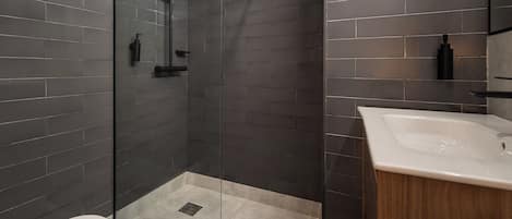 Un baño moderno con ducha de vidrio, tocador de madera y un inodoro.