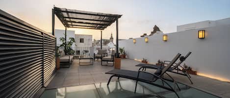 A rooftop terrace with a glass floor, outdoor seating, a pergola, and ambient lighting.