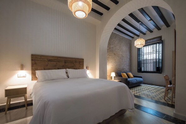 A bedroom with a large bed, a nightstand, a sofa, and a window with a view. - Casa Tomás Boutique Hotel (Seville)