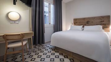 Ein Hotelzimmer mit einem Bett, einem Schreibtisch mit Stuhl, einem an der Wand befestigten Fernseher und einem Fenster mit Vorhängen.