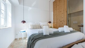 Una habitación de hotel moderna con una cama grande, un panel de madera en la pared, una mesita auxiliar pequeña y una ventana.