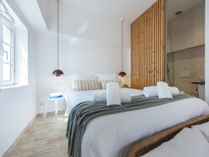 A modern hotel room with a large bed, a wooden panel wall, a small side table, and a window. - Casinha da Esquina - in the heart of Lagos (Lagos)