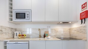 Una cocina moderna con armarios blancos, un microondas integrado, un lavamanos con grifo dorado y una placa de cocina por inducción negra.