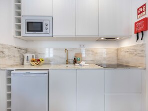 A modern kitchen with white cabinets, a built-in microwave, a sink with a gold faucet, and a black induction cooktop. - Casinha da Esquina - in the heart of Lagos (Lagos)