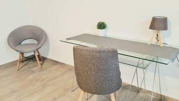 Un espace de bureau moderne avec un bureau en verre, deux chaises grises, une petite plante en pot et une lampe posée sur un support en bois.