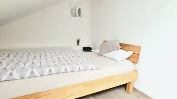 A modern bedroom with a wooden bed frame, a patterned bedspread, and a small potted plant on the nightstand.