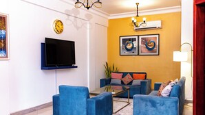Ein Wohnzimmer mit Flachbildfernseher, blauen Sofas, einem Glastisch und Kunstwerken an der Wand.
