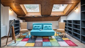 Une chambre aménagée en mezzanine avec un canapé turquoise, deux fauteuils, un tapis coloré et des fenêtres de toit.