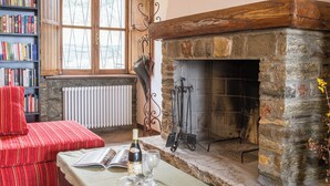 Une pièce chaleureuse avec une cheminée, un canapé rouge, une bibliothèque et une table sur laquelle se trouvent une bouteille et des verres.