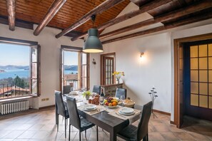 A dining area with a table set for four, a view of the sea, and a wooden ceiling. - Casa Tranquillita Lario (Plesio)