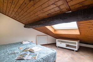 A room with a sloped ceiling, a skylight, a bed with a blue bedspread, a white radiator, and a white storage unit. - Casa Tranquillita Lario (Plesio)