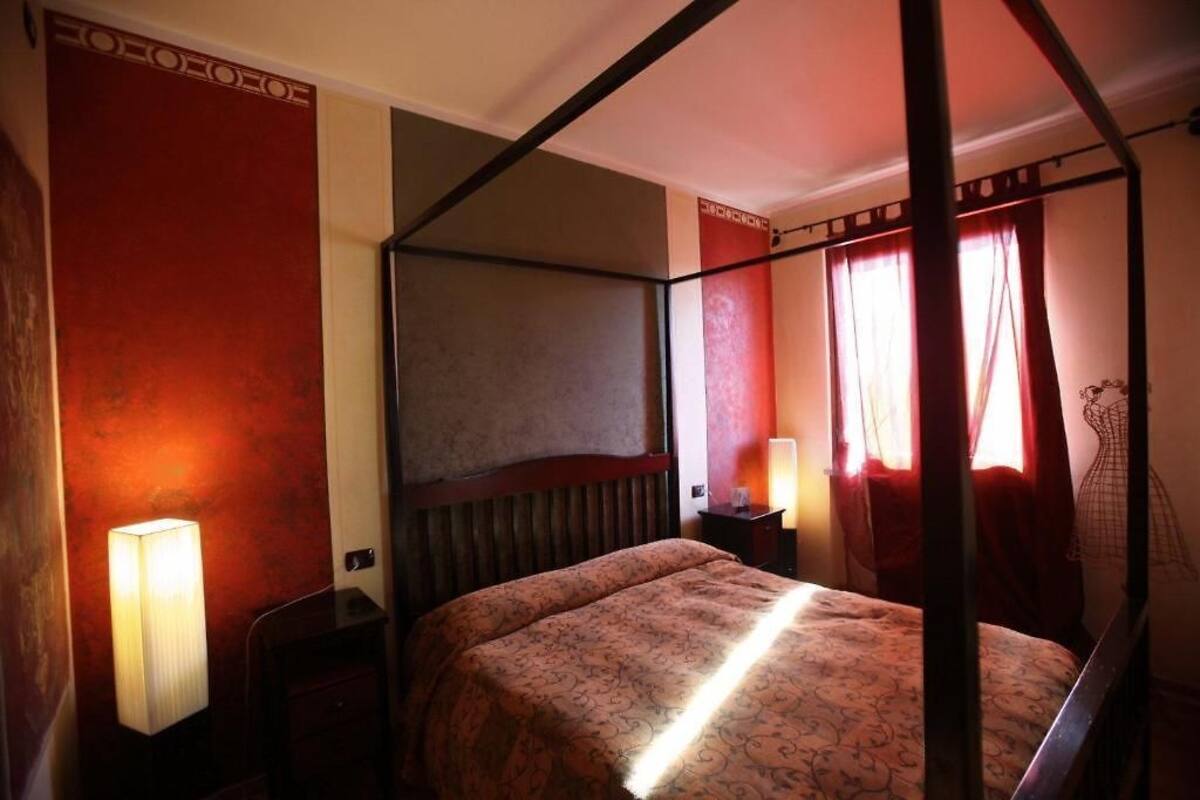 A four-poster bed with a patterned bedspread, a bedside table with a lamp, and a large mirror on the wall.