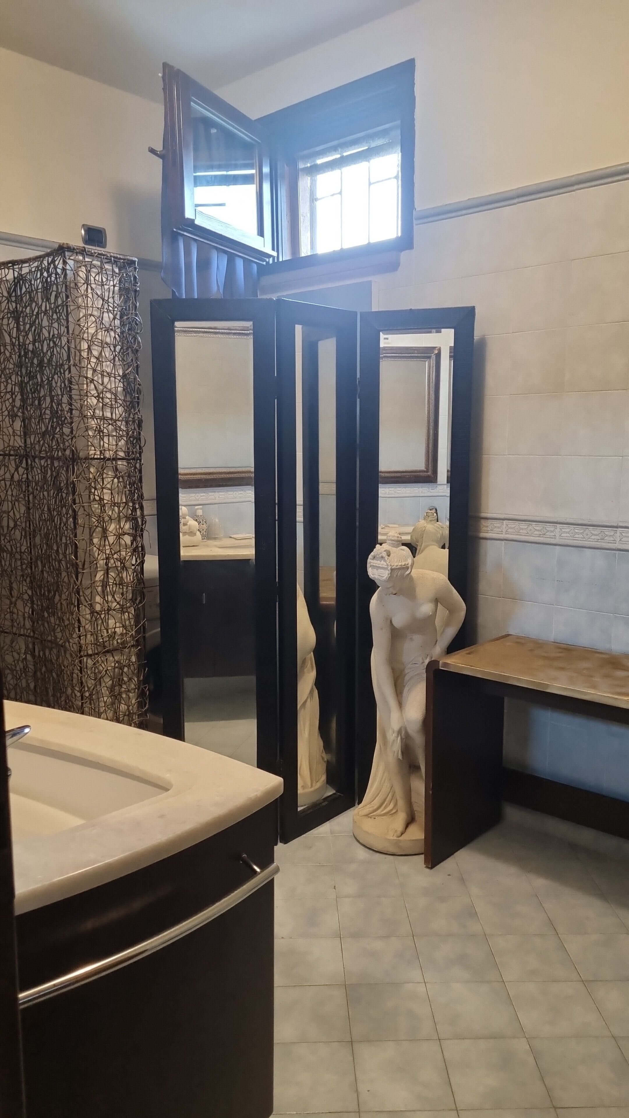 A bathroom with a marble sink, a statue, and a mirror.