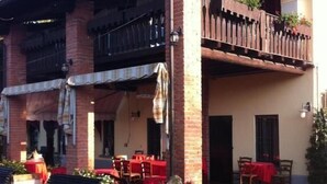 A two-story building with a brick facade, a balcony with a wooden railing, and outdoor seating with tables and chairs. - Manuela Quattro Coppe (San Martino della Battaglia)