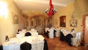A dining area with tables set for a meal, a chandelier, and brick arches in the background. - Manuela Quattro Coppe (San Martino della Battaglia)