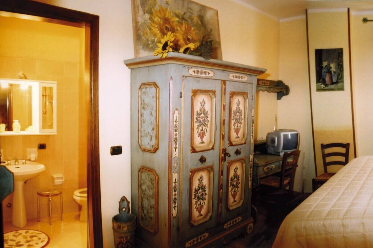 A bedroom with a bed, a dresser, a chair, a television, and a painting on the wall.