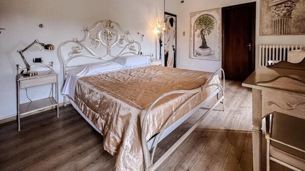 A bedroom with a metal bed frame, a bedside table with a lamp, a dresser, and a wall-mounted radiator. - Manuela Quattro Coppe (San Martino della Battaglia)