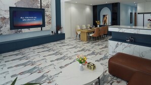 Un interior moderno con televisor, suelo de mármol, una araña, comedor y cocina.