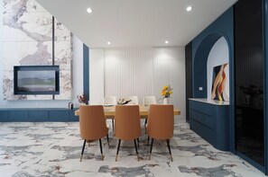 Un comedor moderno con suelo de mármol, un televisor grande montado en la pared y una pared azul con un arco.