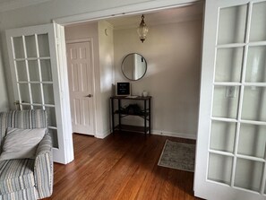 Une pièce avec un canapé à rayures, un plancher en bois, une porte blanche, une petite table avec un miroir et un panneau d’accueil.