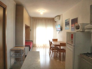 A compact kitchen with a dining area, a microwave, and a TV on the wall. - Cozy Nest Near the Beach (Lignano Sabbiadoro)