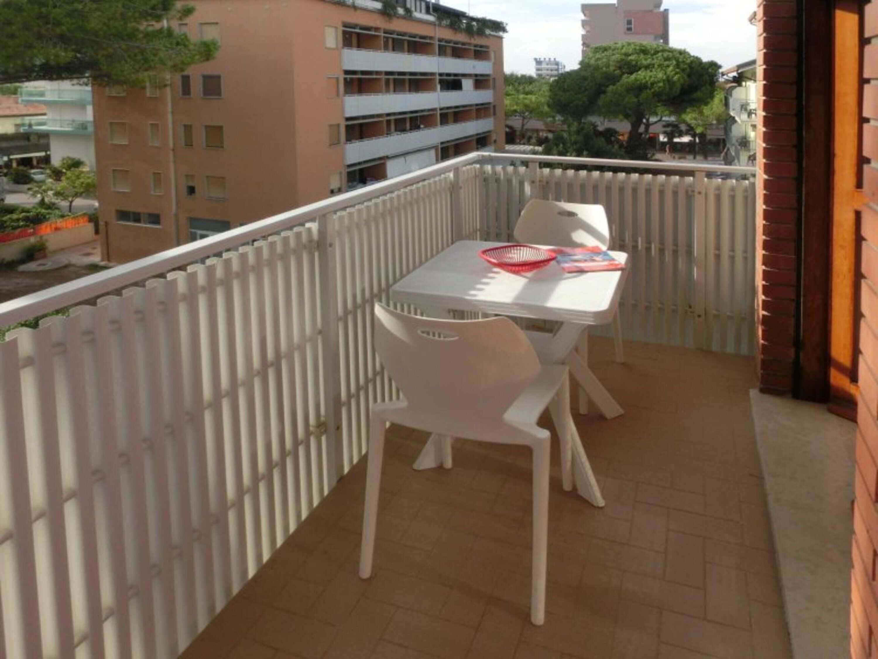A balcony with a table and chairs, a white fence, and buildings in the background.