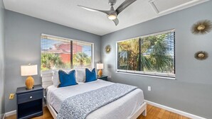 A bedroom with a bed, two bedside tables, a ceiling fan, and two windows with blinds. - Villa Fiesta - 312   “Siesta Key” (Sarasota)