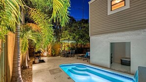A backyard with a swimming pool, palm trees, and a patio area.