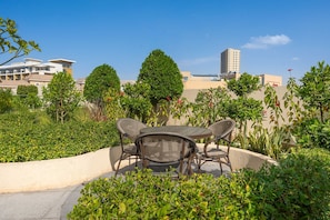 A patio with a round table and chairs, surrounded by greenery and a view of buildings. - Free Housekeeping Visits During Your Stay - Stayshort - Comfortable Studio in JVC That Sleeps 2 (Dubai)