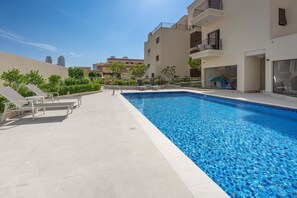 A swimming pool with lounge chairs, a tiled deck, and a building with balconies. - Free Housekeeping Visits During Your Stay - Stayshort - Comfortable Studio in JVC That Sleeps 2 (Dubai)