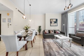 A modern living room with a dining area, grey sofas, a coffee table, and a large window with curtains. - Free Housekeeping Visits During Your Stay - Stayshort - Bright 1 Bedroom Retreat in Dubai Marina That Sleeps 4 (Dubai)