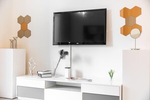Ein modernes Wohnzimmer mit einem an der Wand befestigten Flachbildfernseher, einer weißen Unterhaltungsanlage mit Dekorationselementen und sechseckigen Wandbildern.
