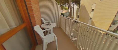 A balcony with a white table and chairs, a brick wall, and a white fence.