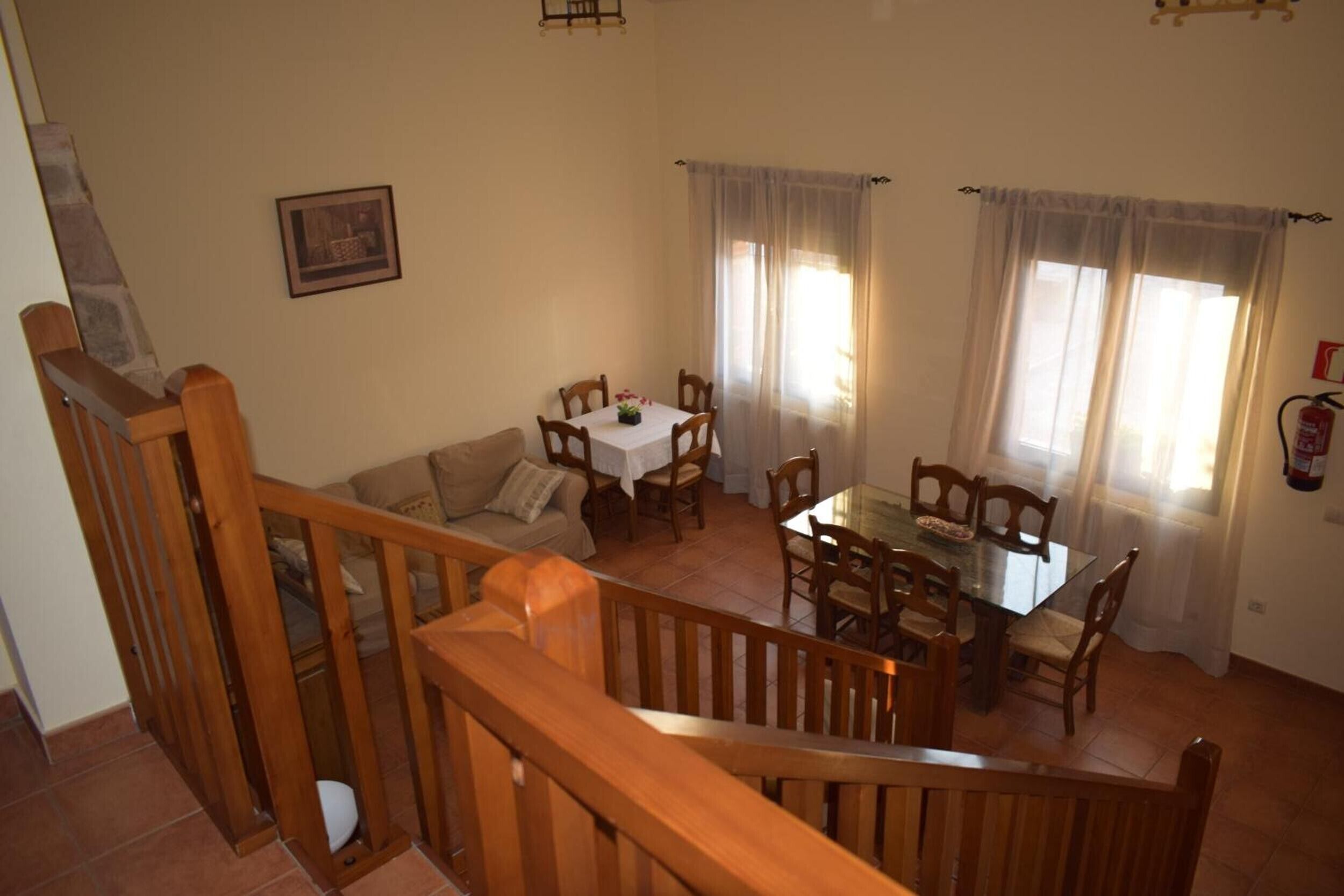 A dining area with a table and chairs, a sofa, a staircase, and a fire extinguisher on the wall.