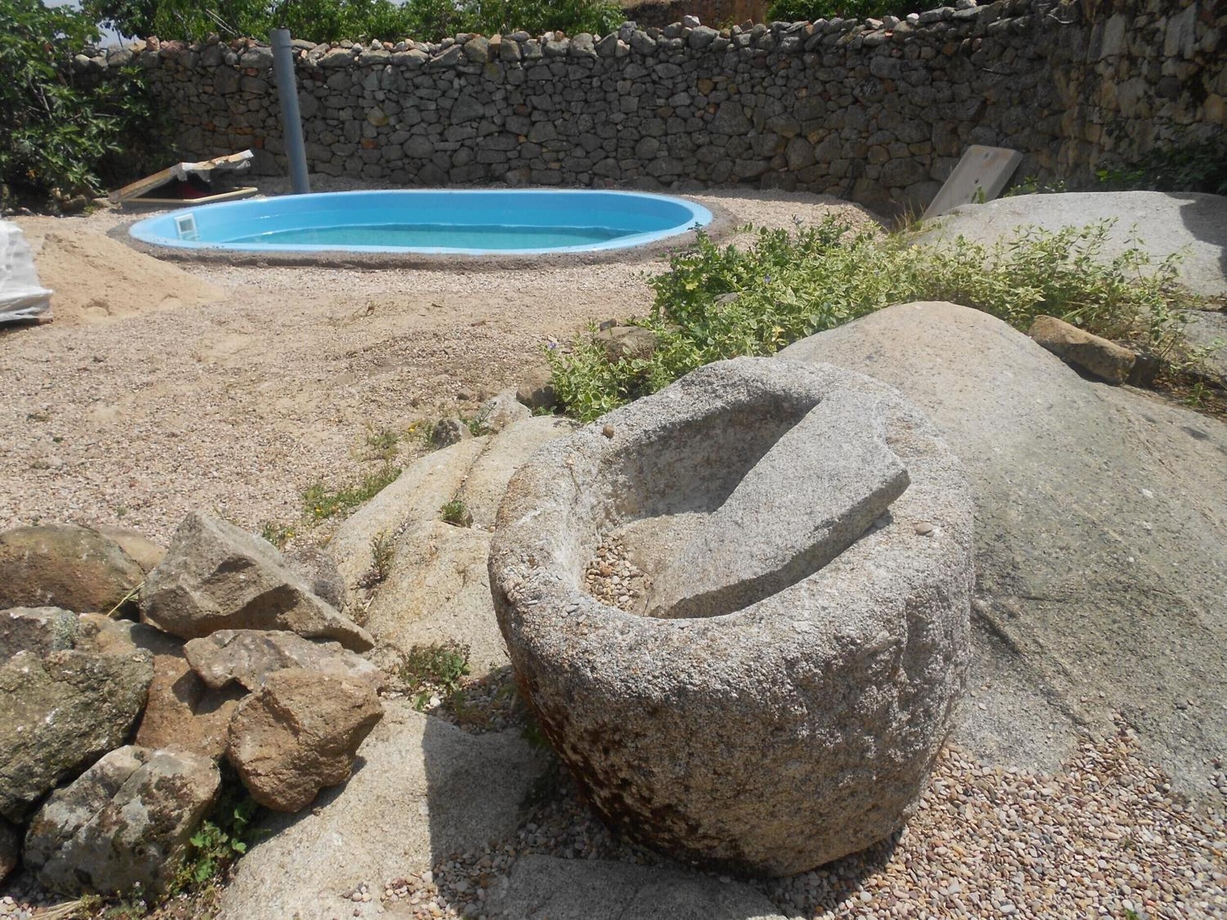 Un muro de piedra, una pequeña piscina y grandes rocas en un entorno natural.