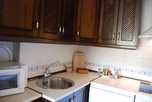 A kitchen with wooden cabinets, a stainless steel sink, a microwave, and a tiled backsplash.