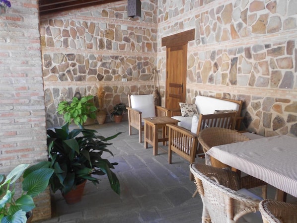 A stone-walled room with a wooden table and chairs, potted plants, and a wooden door.