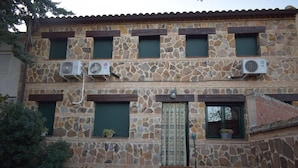 A stone building with multiple air conditioning units, green shutters, and potted plants. - Casa Rural Las Navillas: vistas a la montaña, Wi-Fi y aire acondicionado (Las Navillas)