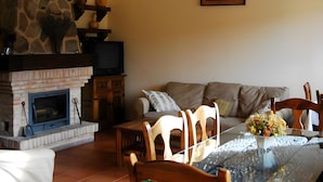 A living room with a stone fireplace, a television, a sofa, and a dining table with chairs. - Casa Rural Las Navillas: vistas a la montaña, Wi-Fi y aire acondicionado (Las Navillas)