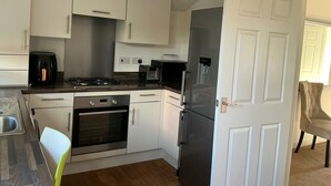 A compact kitchen with white cabinets, a gas stove, a built-in oven, a refrigerator, and a coffee maker. - House Sleeps 8 With Wifi (Dartford)