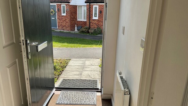 A doorway leading to a residential street with a brick house, a doormat, and a radiator. - House Sleeps 8 With Wifi (Dartford)