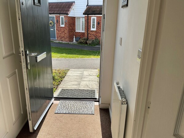 Una puerta que da a una calle residencial con una casa de ladrillo, un felpudo y un radiador.