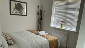 A bedroom with a bed, a radiator, a window with blinds, a framed picture on the wall, and a potted plant on the windowsill. - House Sleeps 8 With Wifi (Dartford)