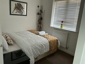 Un dormitorio con cama, un radiador, una ventana con persianas, un cuadro en la pared y una planta en maceta en el alféizar.