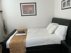 Un lit bien fait, avec une couvre-lit à motifs, une tête de lit sombre et un tableau encadré accroché au mur.
