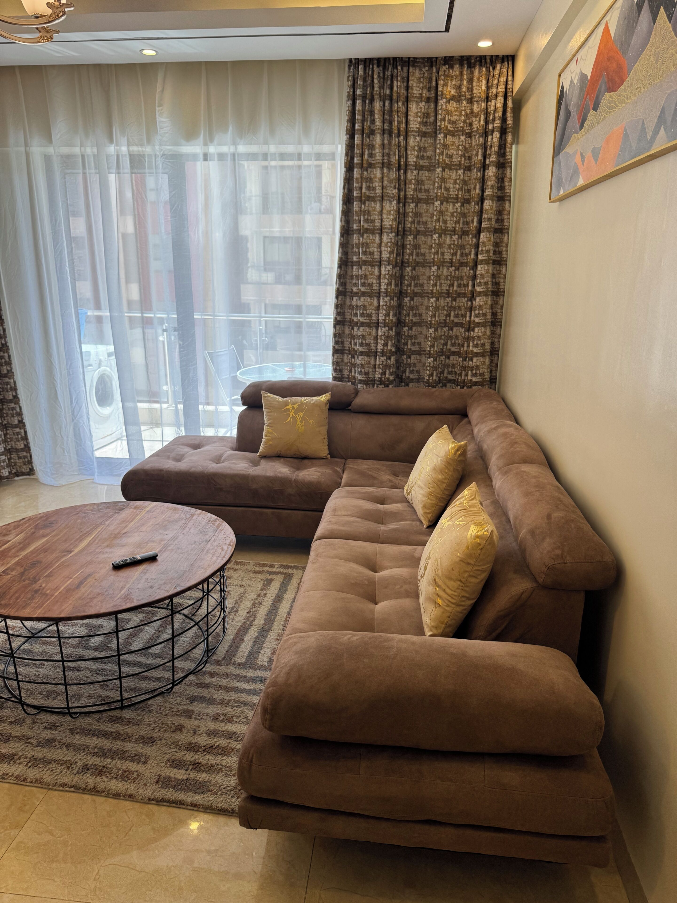 A modern living room with a sectional sofa, a round coffee table, and a view through large windows.