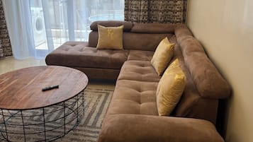 A modern living room with a sectional sofa, a round coffee table, and a view through large windows.
