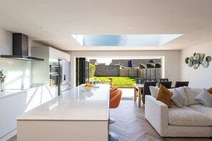 Eine moderne Küche mit einer großen Kochinsel, einem Essbereich mit einer Couch und Blick auf einen Garten.