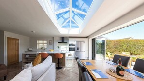 A modern kitchen with a skylight, dining area with a table set for two, and a view of the outdoors. - Stylish Coastal 3BD Bungalow with Garden (West Wittering)